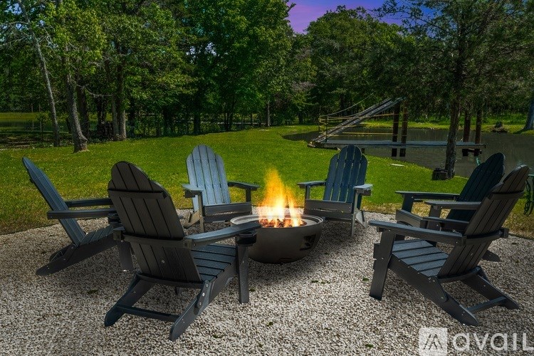 A fire pit surrounded by Adirondack chairs in a gravel area.