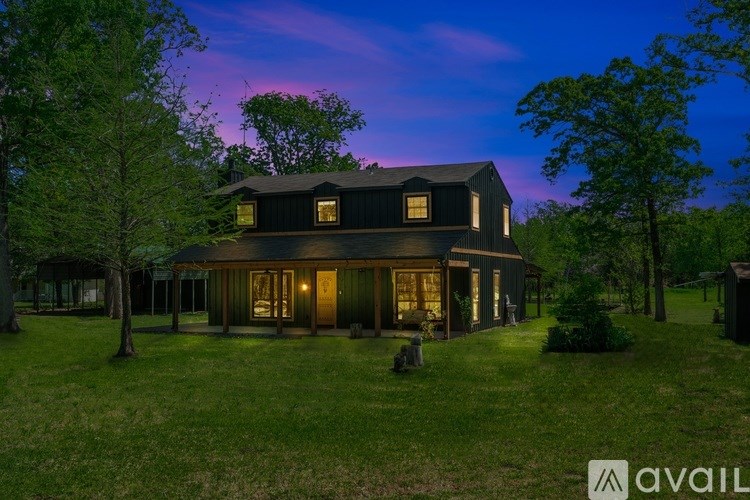 A house with a dark roof and lit windows is surrounded by trees.