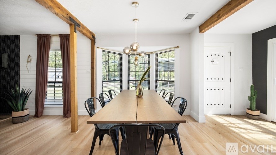 A long wooden table is surrounded by chairs in a room with a large window.