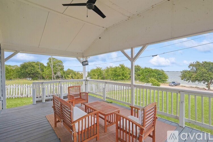 A wooden table and chairs are set up on a covered deck with a view of the water.