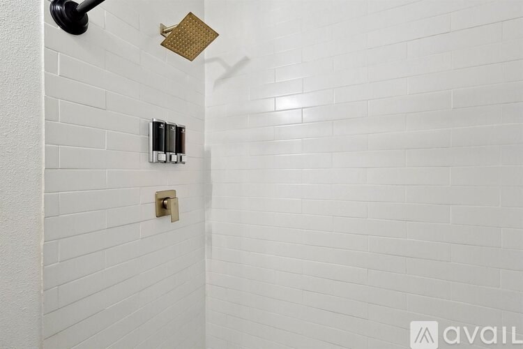 A white tiled shower with a gold shower head and a silver faucet.