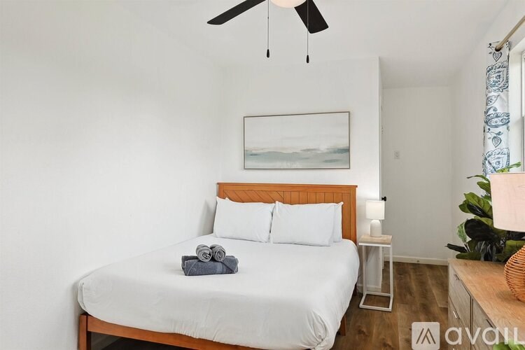 A bedroom with a bed, a ceiling fan, and a painting on the wall.