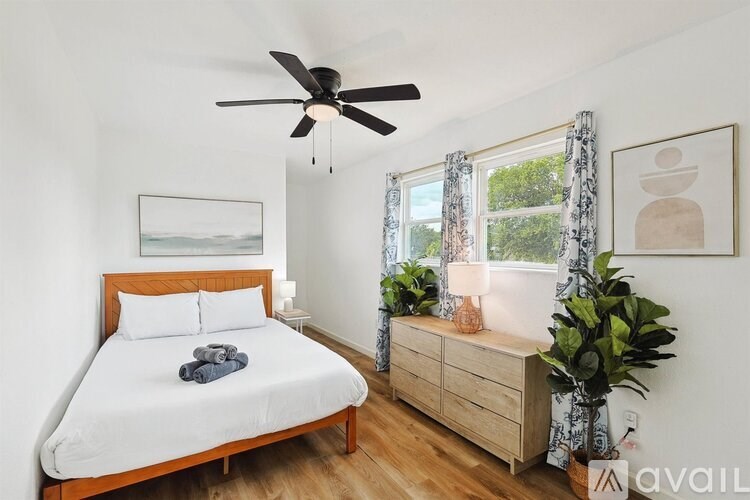 A bedroom with a bed, a dresser, a ceiling fan, and a window with curtains.