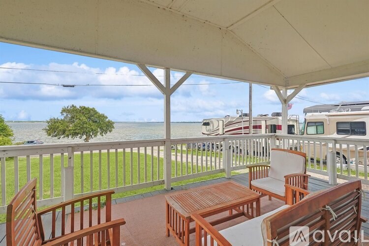 A patio with wooden furniture and a white canopy overlooking a body of water.