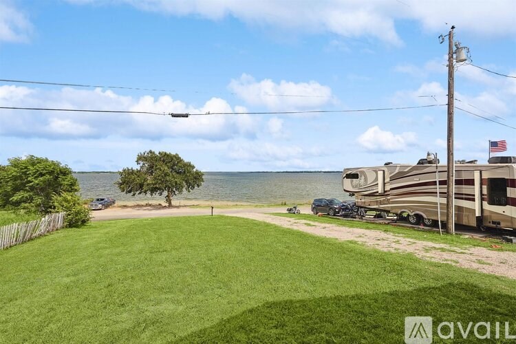 A grassy area with a fence, a tree, and a houseboat on the water.