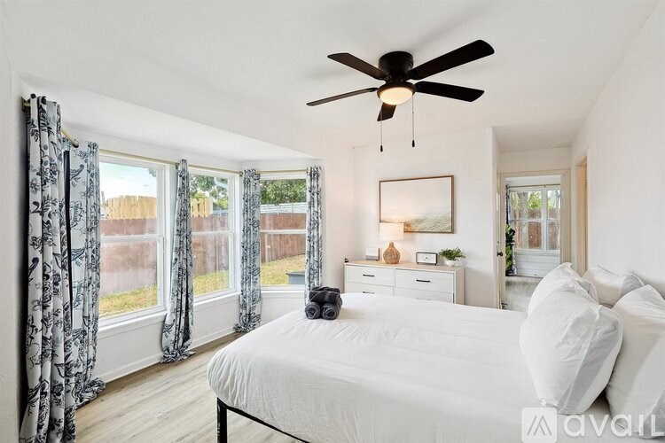 A bedroom with a large bed, a ceiling fan, and a window with curtains.