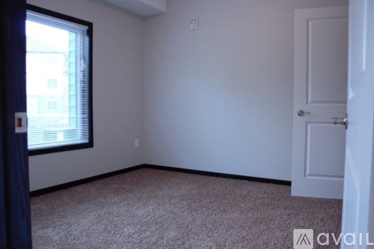 A room with a carpeted floor, a door, and a window with blinds.