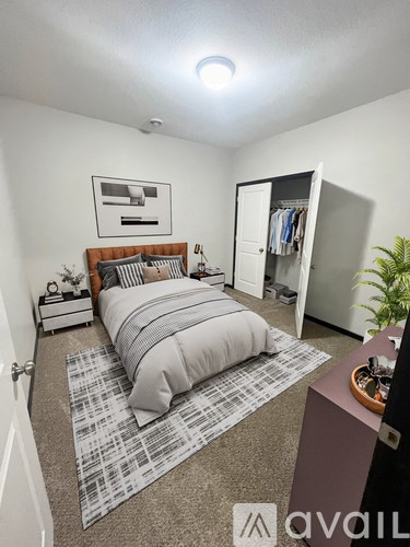 A bedroom with a bed, nightstand, and a plant.