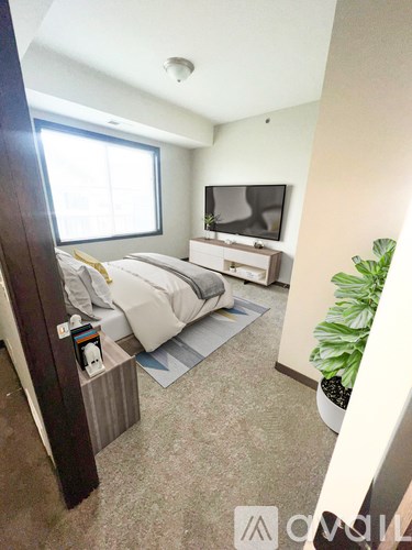 A bedroom with a bed, nightstand, and a TV on the wall.