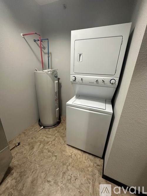A small white washing machine sits next to a tall white container.