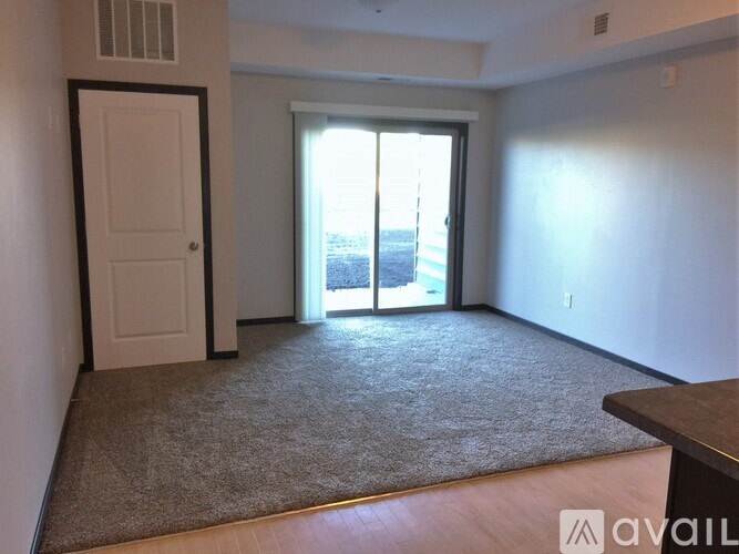 A room with a carpeted floor, a white door, and a large window with a view of the outside.
