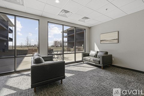 A living room with two grey couches and a large window overlooking a parking lot.
