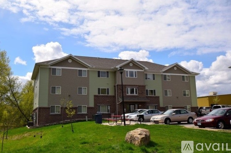 Apartment complex with a grassy area in front and cars parked in the driveway.