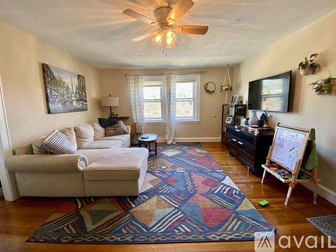 A living room with a couch, a rug, a fan, and a painting on the wall.