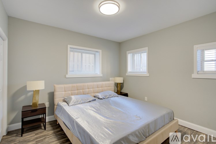 A bedroom with a bed, nightstand, and two windows.