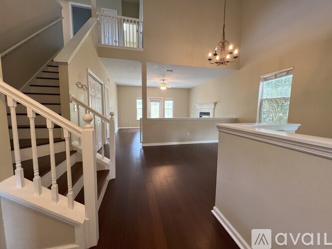A spacious living room with a staircase on the left and a chandelier hanging from the ceiling.