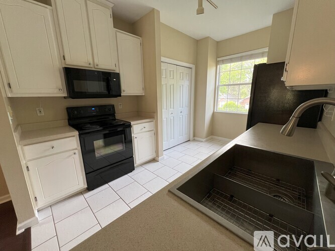 A kitchen with white cabinets and black appliances is available for rent.