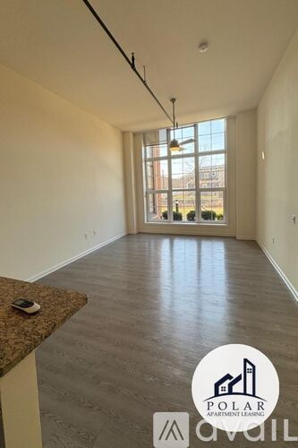 A spacious room with a large window and a view of a fence and trees outside.