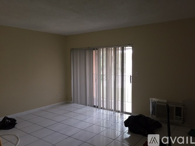 A room with a large window covered by white blinds and a black bag on the floor.