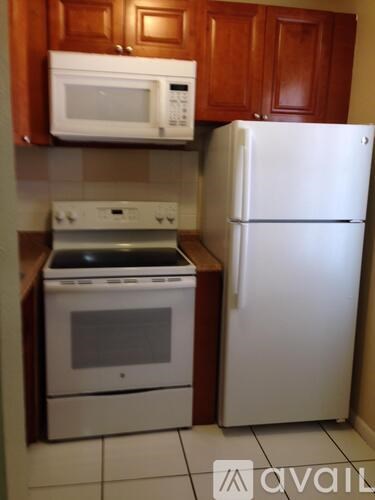 A white refrigerator stands next to a white microwave and an oven in a kitchen.