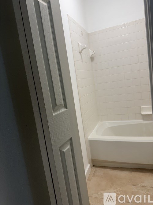 A white tiled bathroom with a bathtub and a door.