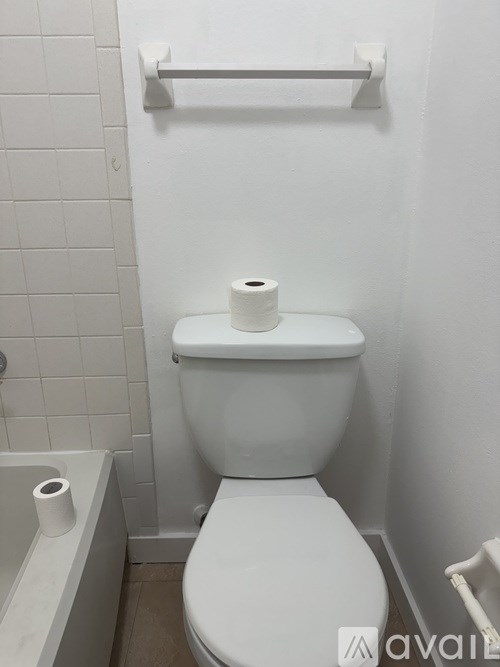 A white toilet with a roll of toilet paper on top of it.