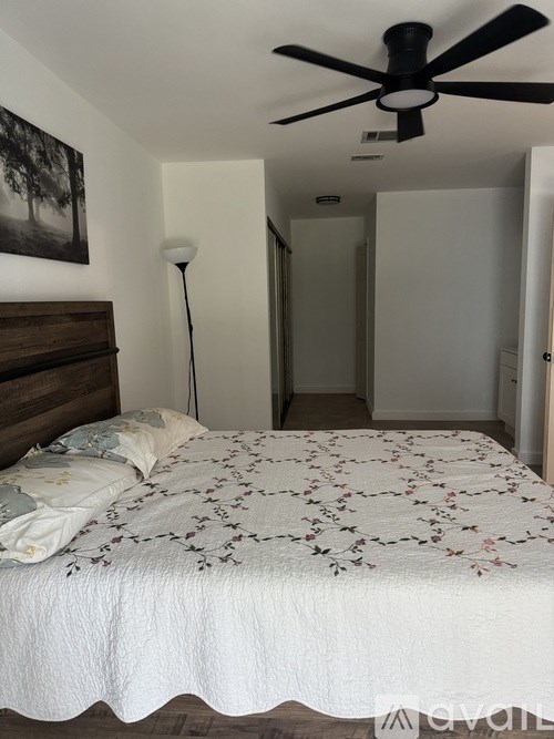 A bedroom with a bed, a ceiling fan, and a painting on the wall.