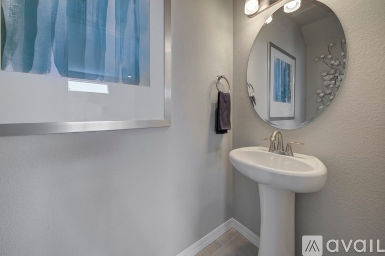 A bathroom with a white pedestal sink and a round mirror.