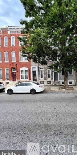 A white car is parked on the street in front of a red building.