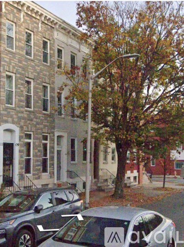 A tree with orange leaves stands next to a building with a white door.
