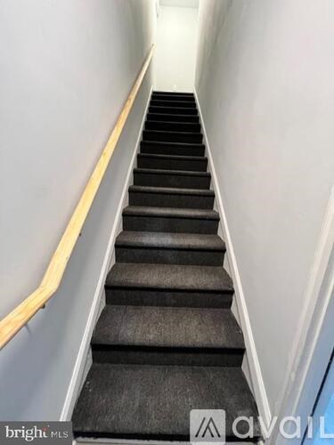 A staircase with black carpeted steps and a wooden handrail.