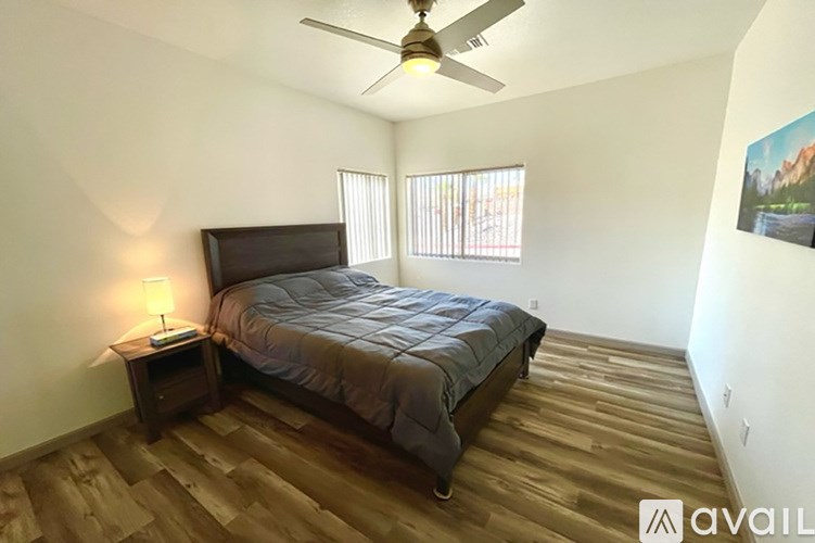 A bedroom with a bed, a ceiling fan, and a wooden floor.