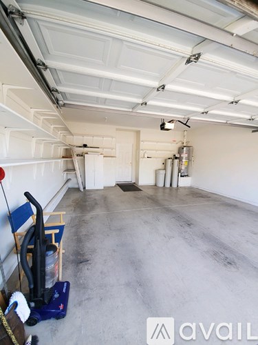 A large, empty garage with a blue vacuum cleaner on the left side.