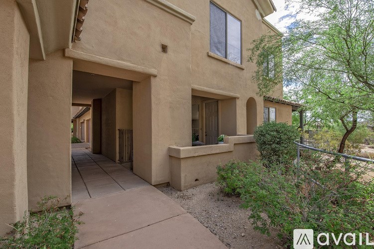A beige house with a balcony and a tree in front.