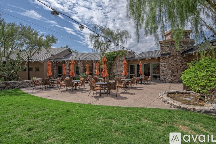 A patio with tables and chairs is surrounded by a grassy area and a stone wall.
