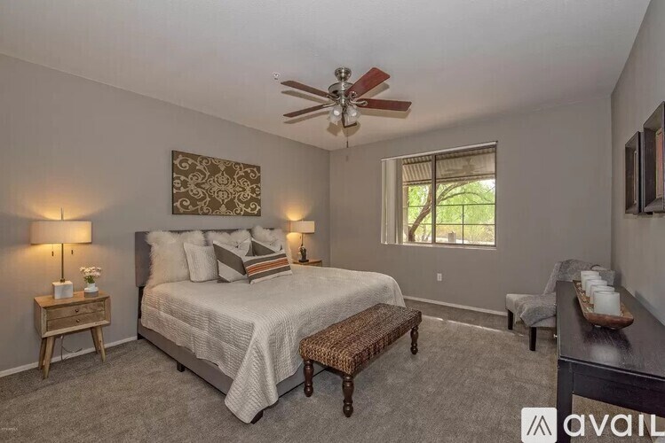 A bedroom with a large bed, a ceiling fan, and a window with a view of trees.
