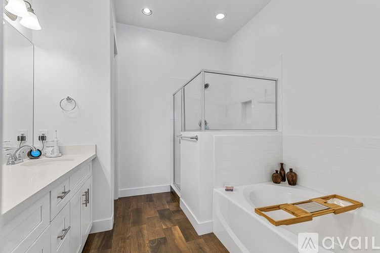 A white bathroom with a wooden floor and a white tub.