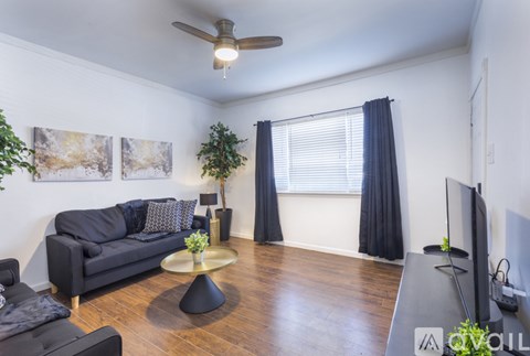 A living room with a black couch, a coffee table, and a ceiling fan.