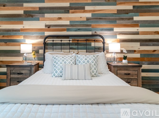 A bed with a white comforter and two decorative pillows sits in front of a wooden wall.