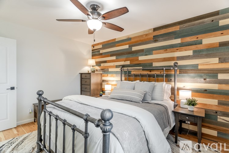 A bedroom with a bed, a ceiling fan, and a wooden wall paneling.