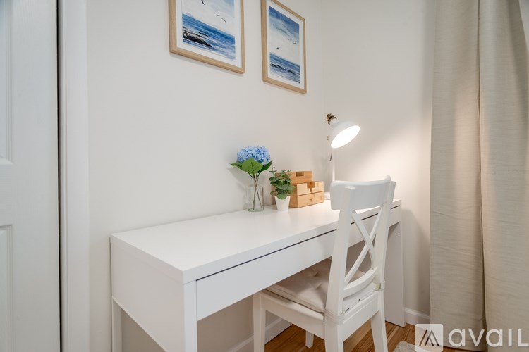 A white desk with a white chair and a vase of blue flowers on top.