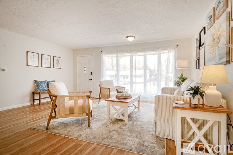 A living room with a white sofa, a wooden chair, and a white table with a plant on it.