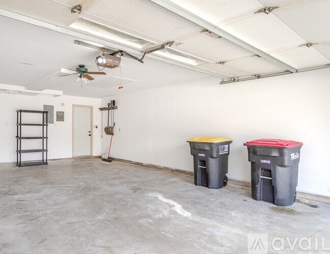 A room with a fan, two trash cans, and a broom.