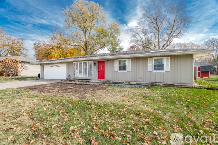 A house with a red door is surrounded by fallen leaves.