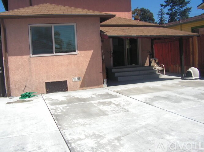 A house with a brown roof and a pink wall with a white window and a white chair outside.
