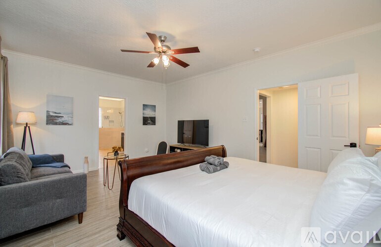 A bedroom with a large bed, a grey couch, a ceiling fan, and a painting on the wall.