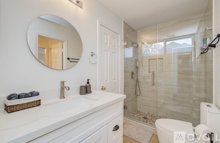 A white bathroom with a round mirror and a white toilet.