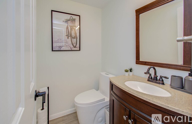 A bathroom with a toilet, sink, mirror, and a picture of a bicycle on the wall.