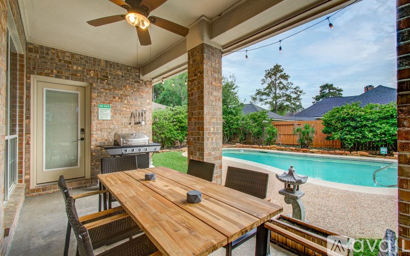 A wooden table is set on a patio with a ceiling fan and a pool in the background.