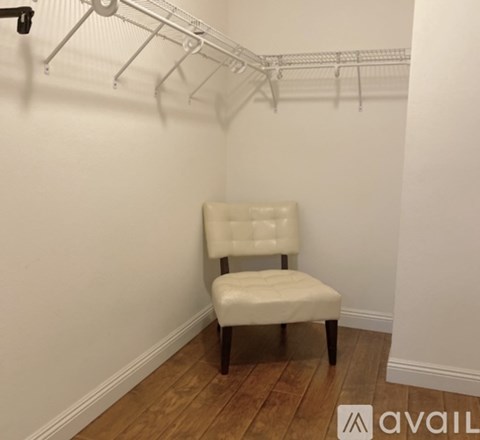 A white chair with wooden legs sits in a room with a white wall and a clothes rack.